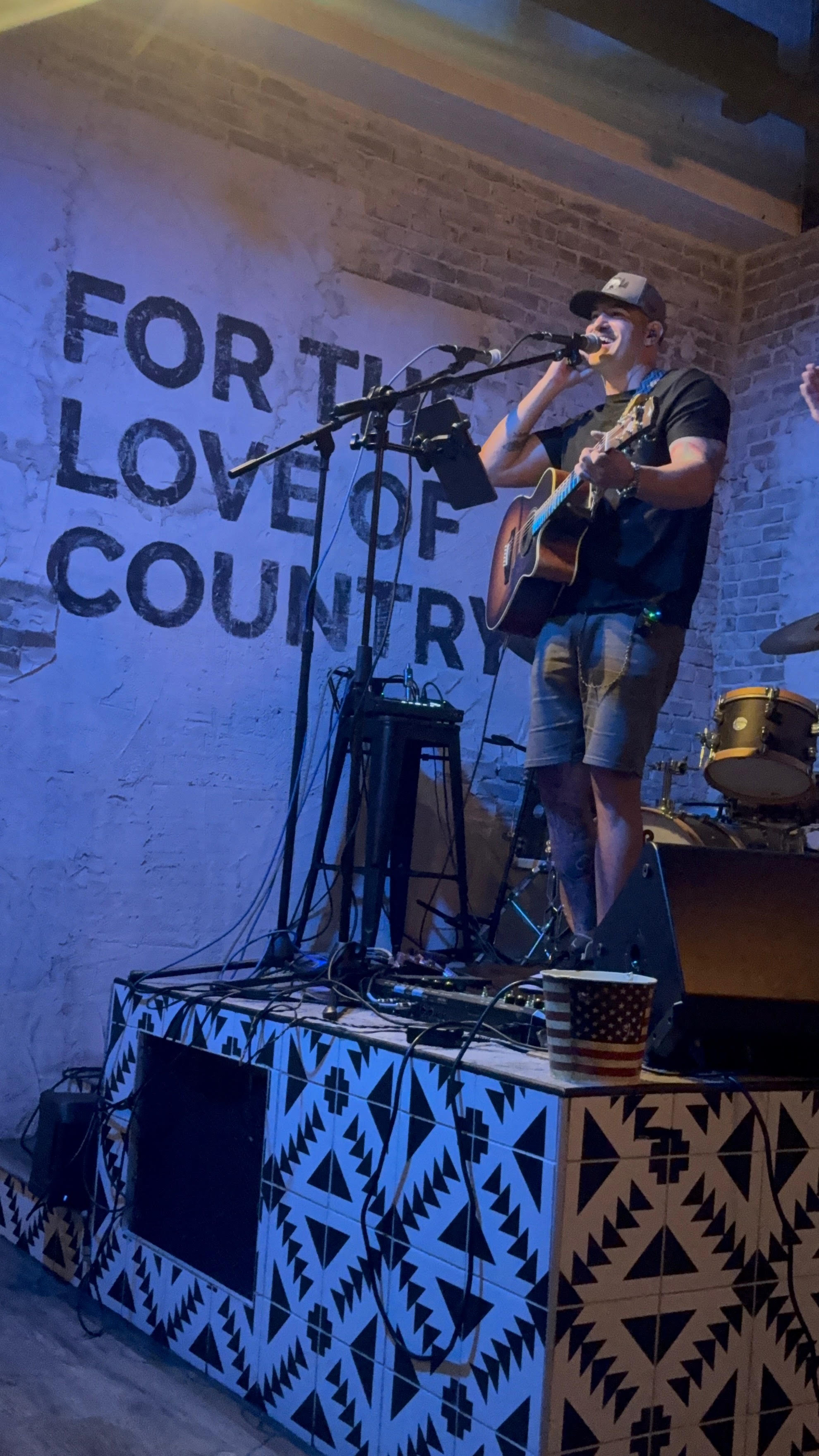 Justin Kennett performing live on stage, singing into the microphone while playing guitar under blue stage lighting